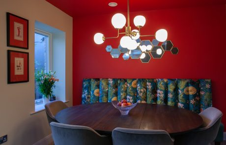 Dining room with red wall & ceiling, floral custom banquette seat, extendable dining table, pendant light & mirror